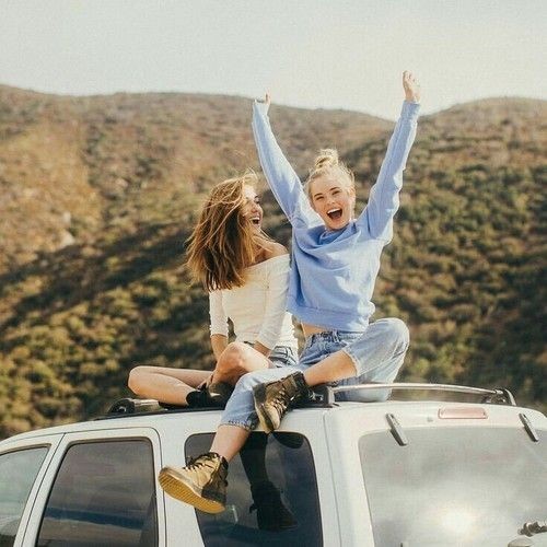 Two happy girls sitting on a car feeling free and alive